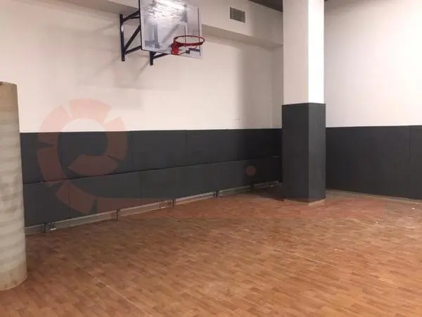 Тёмно-серые стеновые протекторы в школьном спортзале с баскетбольным щитом и паркетным полом