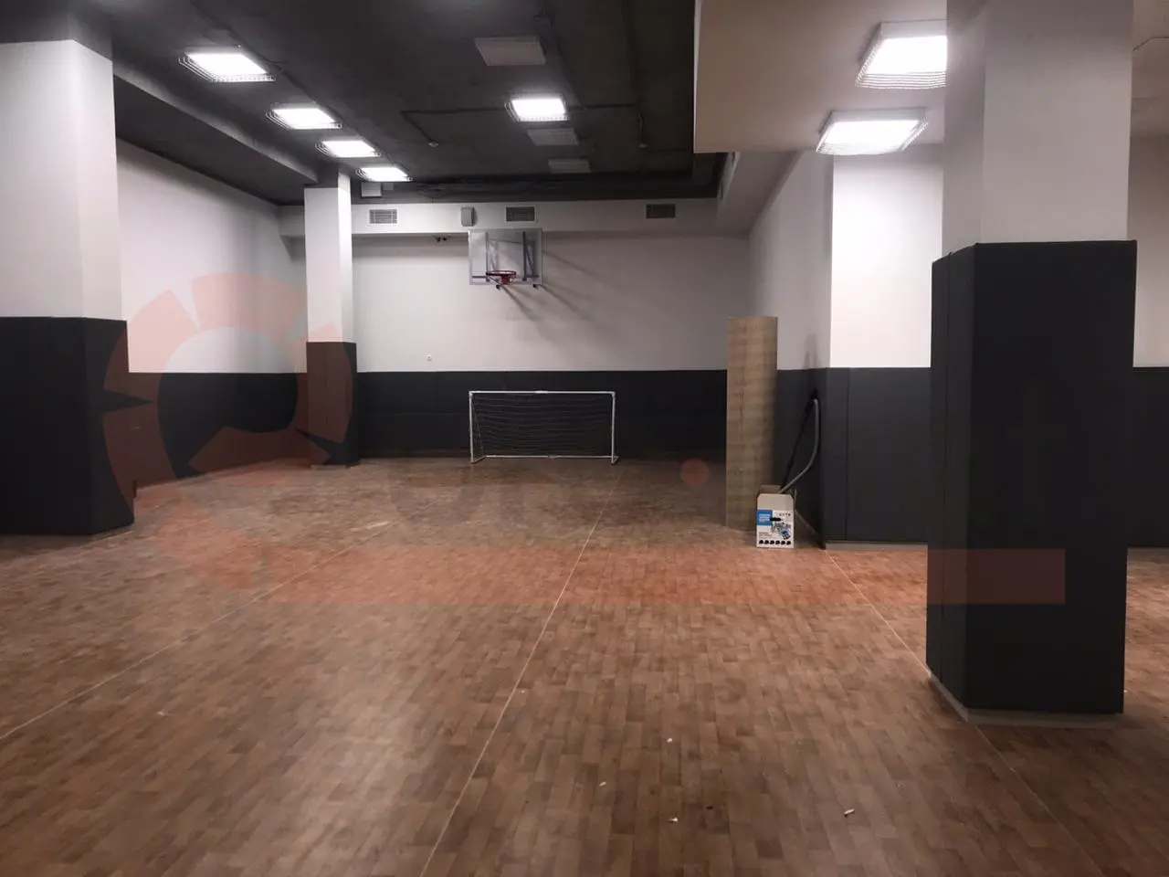 Панорамный вид школьного спортзала с тёмно-серыми стеновыми протекторами, баскетбольным щитом и воротами