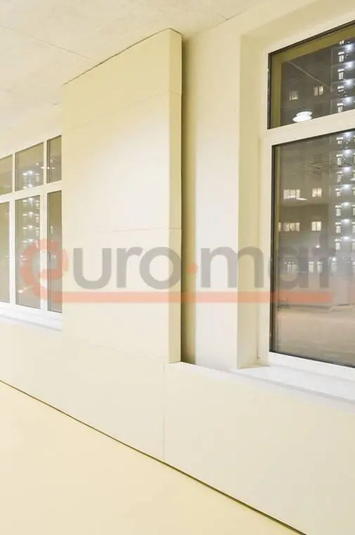 Белые стеновые протекторы между окнами в школьном зале с бежевыми стенами, вечернее время