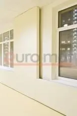 Белые стеновые протекторы между окнами в школьном зале с бежевыми стенами, вечернее время