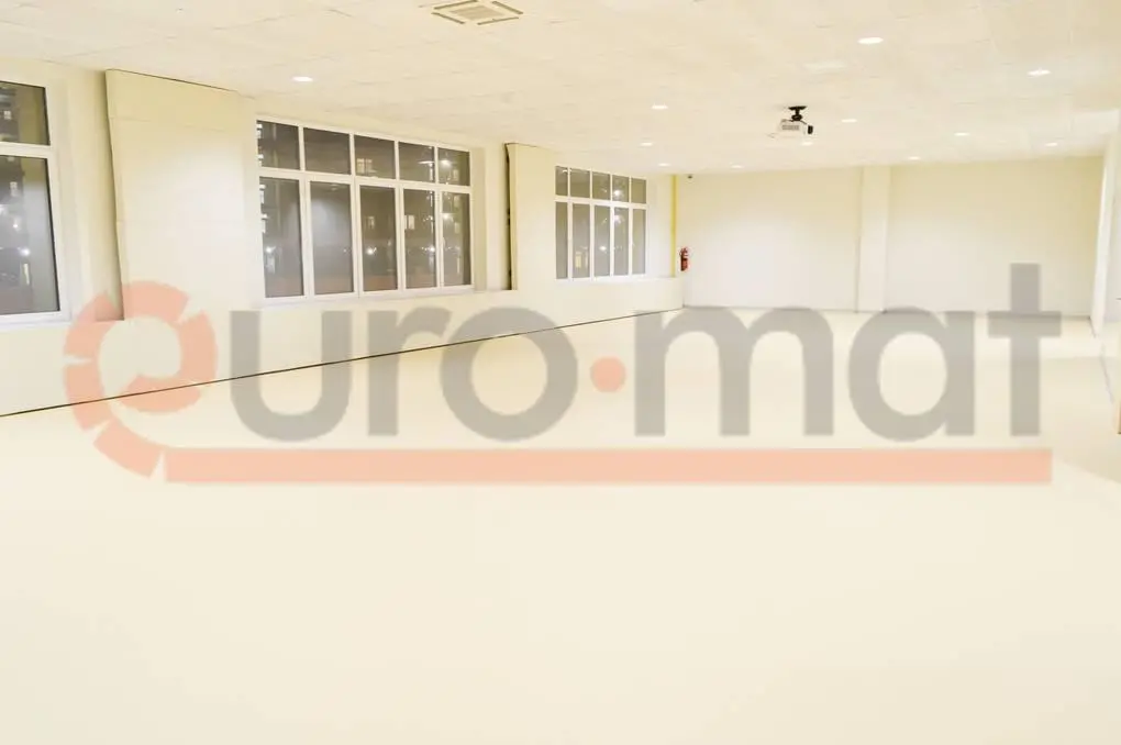 Белые стеновые протекторы и светло-бежевое напольное покрытие в просторном школьном зале с окнами