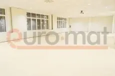 Белые стеновые протекторы и светло-бежевое напольное покрытие в просторном школьном зале с окнами