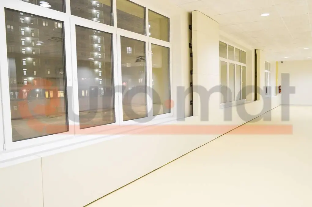 Белые стеновые протекторы вдоль оконной стены школьного зала с бежевым напольным покрытием