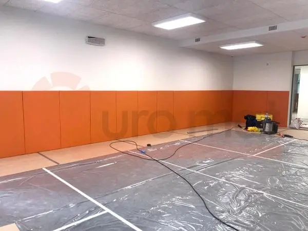 Монтаж оранжевых стеновых протекторов в спорткомплексе — панели вдоль стены, пол защищён плёнкой