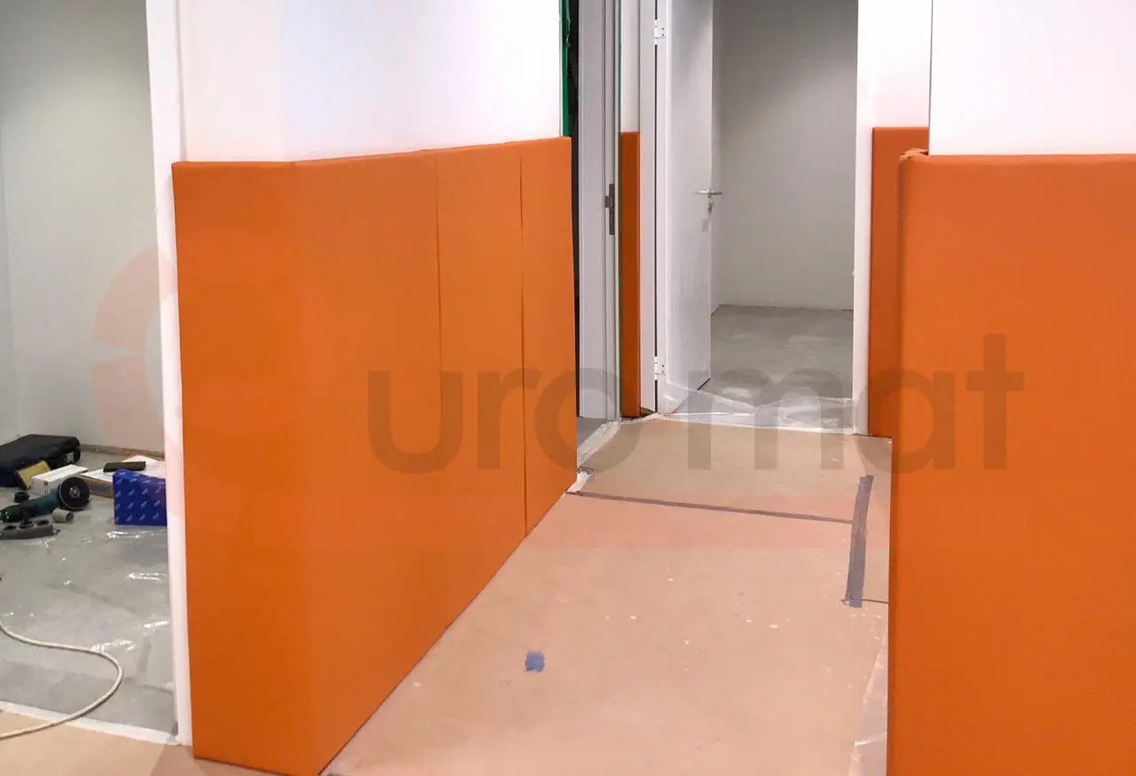 Монтаж оранжевых стеновых протекторов в коридоре спорткомплекса, процесс установки