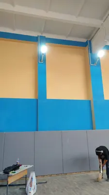 Монтаж серых стеновых протекторов в спортзале Владикавказа, рабочий крепит панель на стену