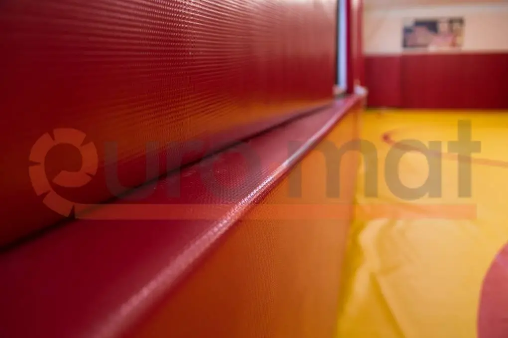 Красные стеновые протекторы крупным планом, жёлтый борцовский ковёр на заднем плане