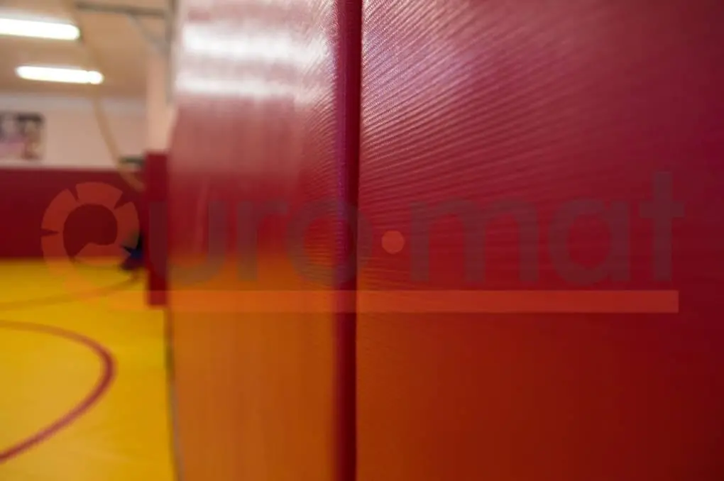 Красные стеновые протекторы крупным планом с жёлтым борцовским ковром на заднем плане