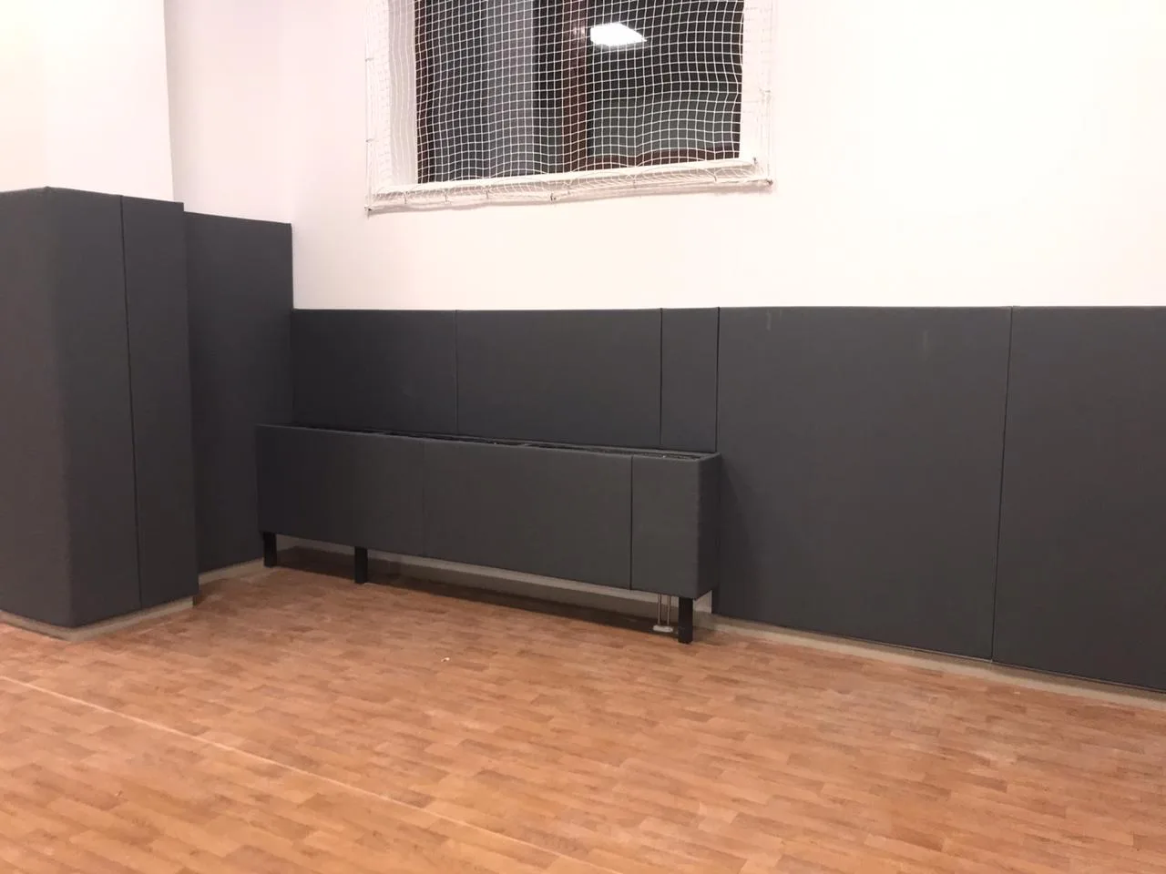 Фото 5: тёмно-серые стеновые протекторы вдоль стены спортзала с защитной сеткой у окна