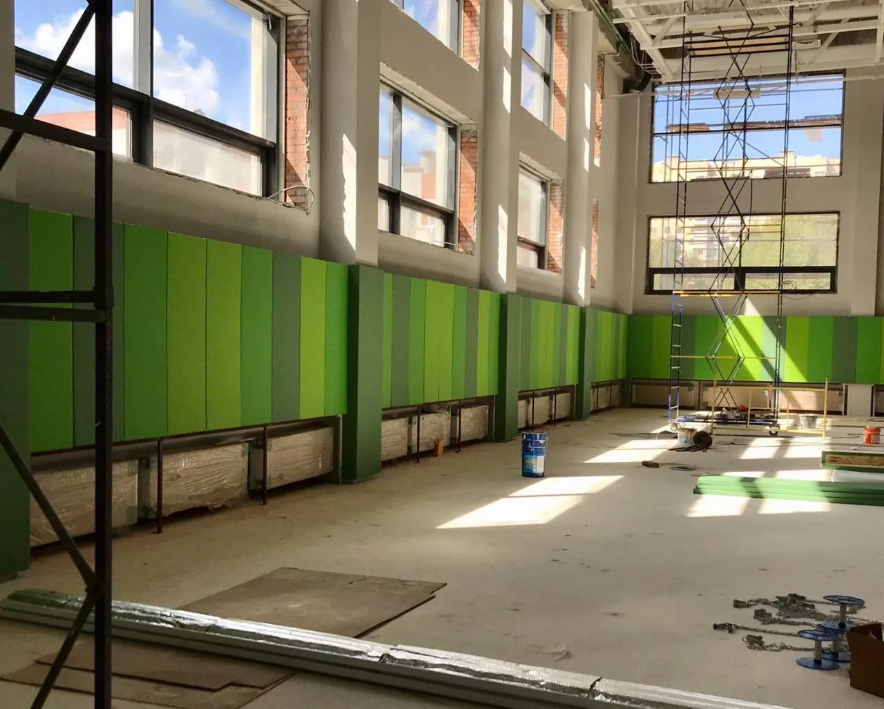 Установленные зелёные протекторы вдоль стены спортзала с окнами и строительными лесами