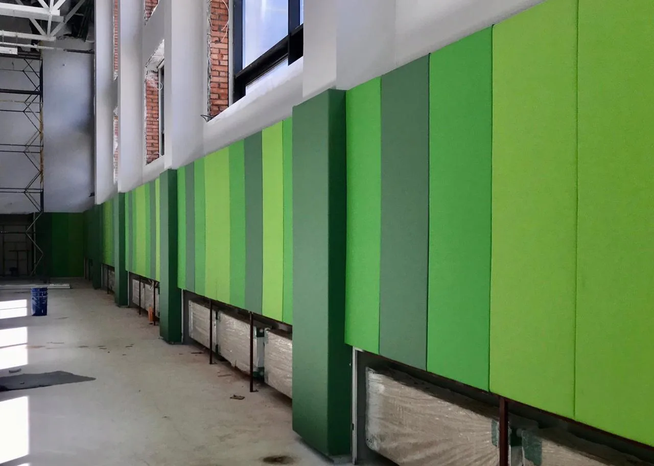 Установленные зелёные стеновые протекторы в разных оттенках вдоль стены с окнами и батареями