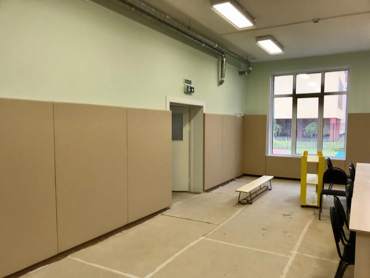 Бежевые стеновые протекторы на стенах зала детского сада с дверью и окном