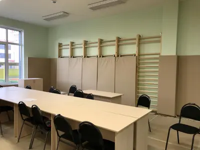 Бежевые протекторы за шведской стенкой в спортзале детского сада с партами и стульями