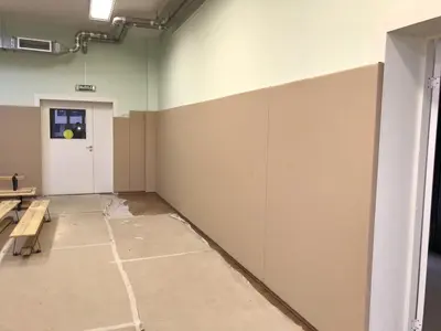 Бежевые стеновые протекторы вдоль длинной стены зала детского сада с дверью