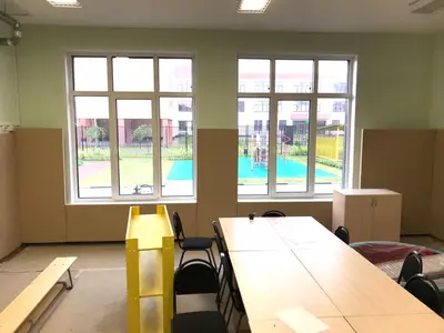 Бежевые протекторы под окнами с видом на детскую площадку в зале детского сада