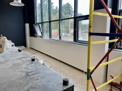 Светлые протекторы под подоконником в строящемся школьном спортзале со строительными лесами