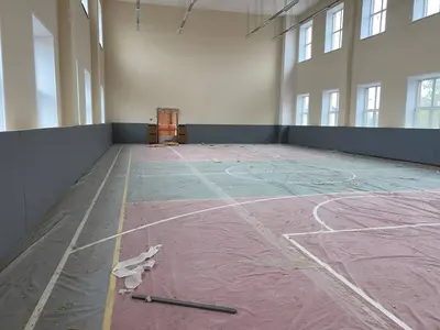 Серые стеновые протекторы вдоль длинной стены школьного спортзала с окнами