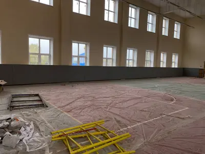 Серые протекторы вдоль длинной стены спортзала с окнами и строительными лесами