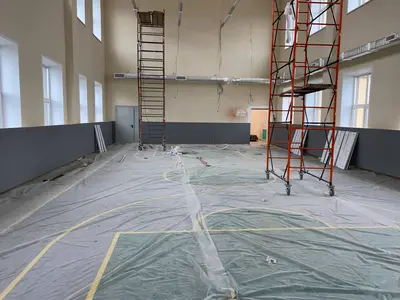 Серые стеновые протекторы на торцевой стене школьного спортзала со строительными лесами