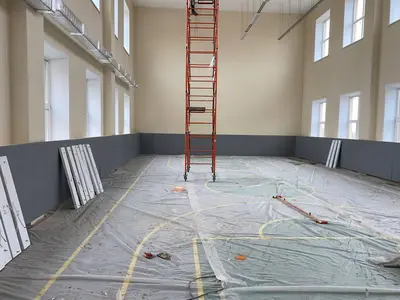 Серые протекторы по периметру школьного спортзала, вид на три стены с окнами