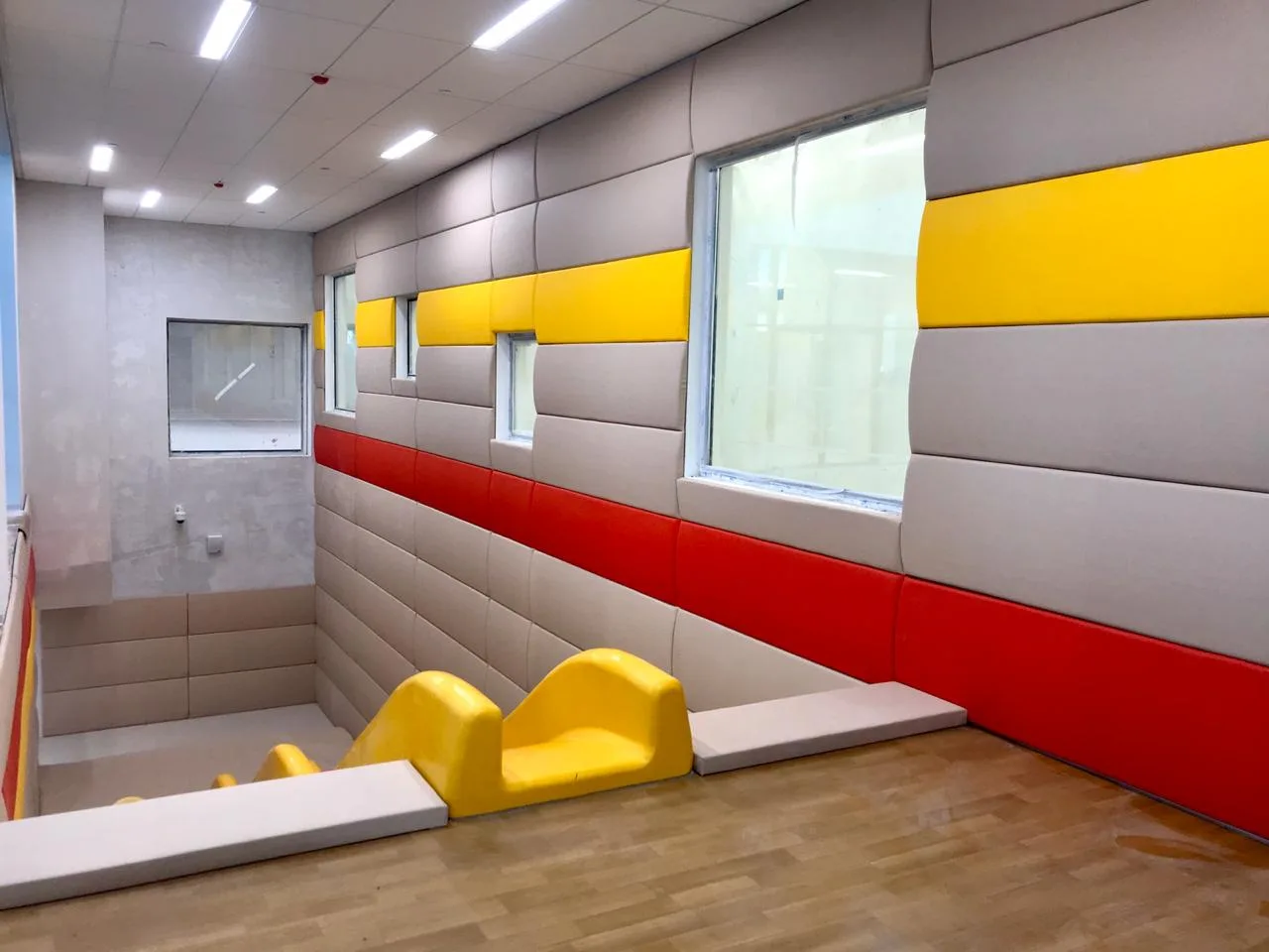 Выпуклые протекторы бежевого, жёлтого и красного цвета вдоль стены с окнами в игровой зоне