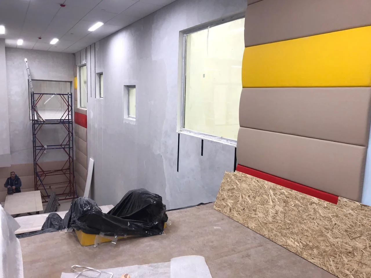 Процесс монтажа выпуклых бежевых и жёлтых протекторов на стены с лесами и инструментами