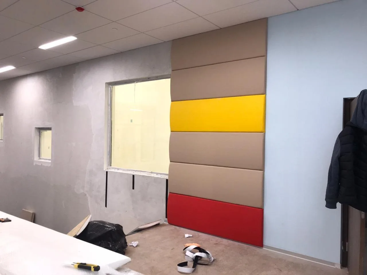 Выпуклые бежевые, жёлтые и красные стеновые протекторы у окна крупным планом в процессе монтажа