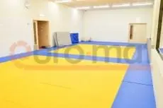 Татами жёлтого и синего цвета уложены на полу зала дзюдо с видимыми стыками пазлов