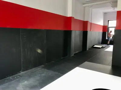 Чёрные татами и красно-чёрные протекторы в зале Kaylas Team Junior — вид на дальнюю стену