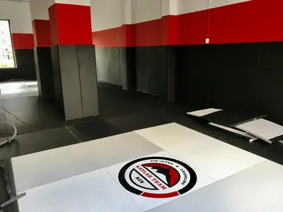 Логотип Kaylas Team Jiu-Jitsu & Grappling на чёрных татами с красно-чёрными протекторами на стенах